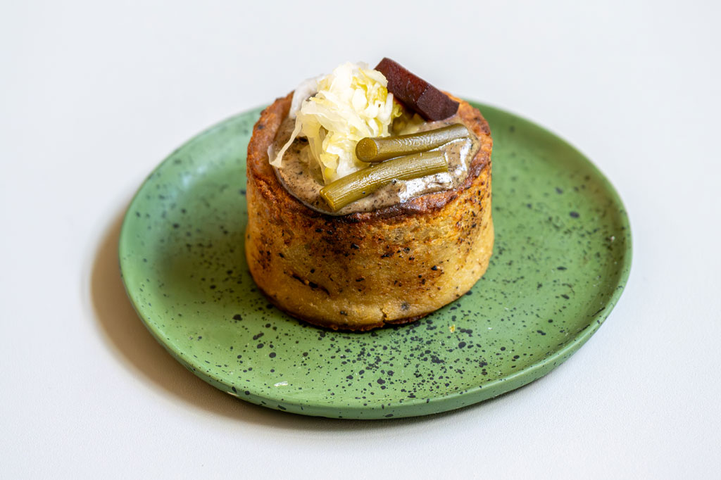 Na zielonym talerzu babka ziemniaczana udekorowana kapustą kiszoną, burakiem i zieloną fasolką