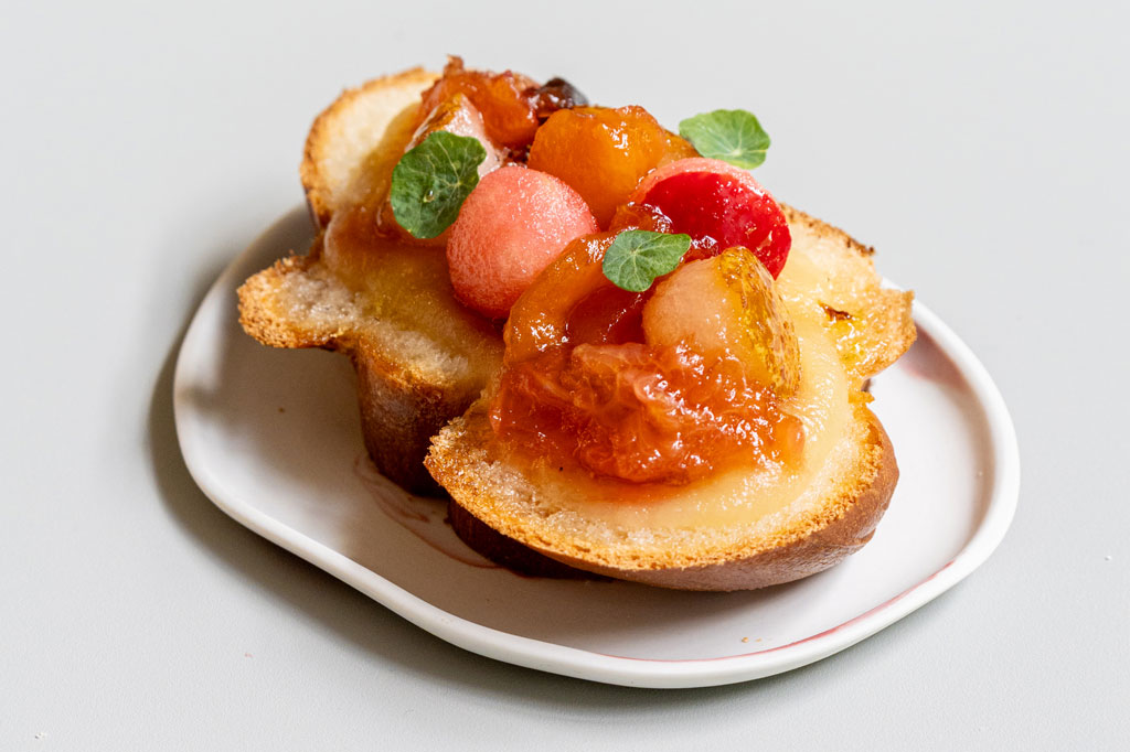 Na białym talerzyku gruby plaster chałki, na niej owoce