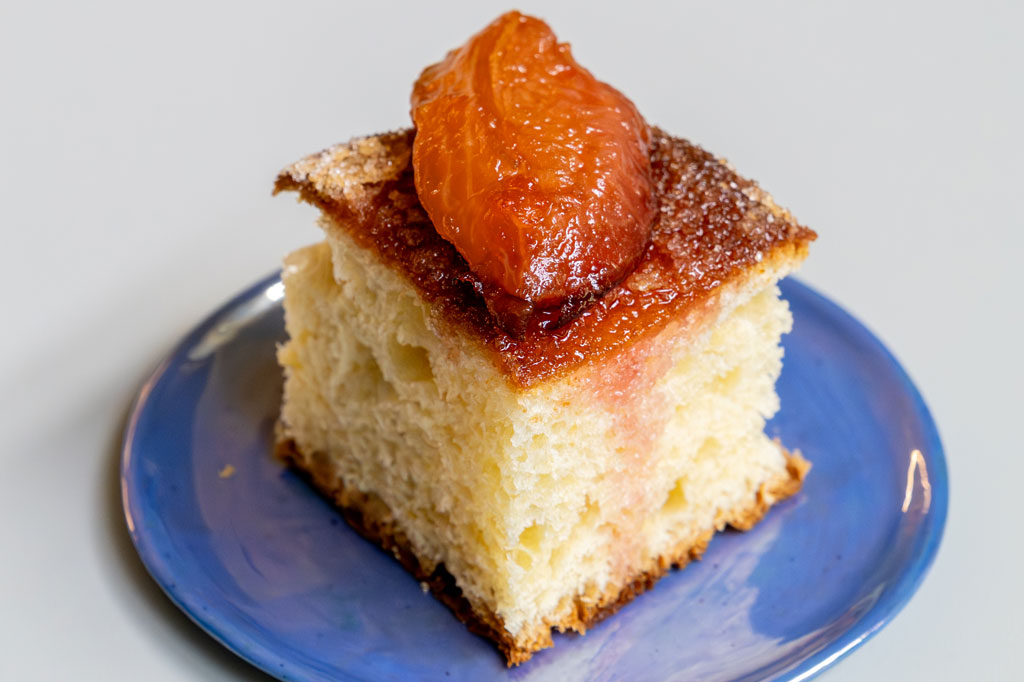 Na niebieskim talerzyku kawałek ciasta drożdżowego z owocem na górze