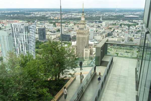 Taras widokowy na budynku Varso, drzewa, ławki, ludzie oglądają panoramę miasta.