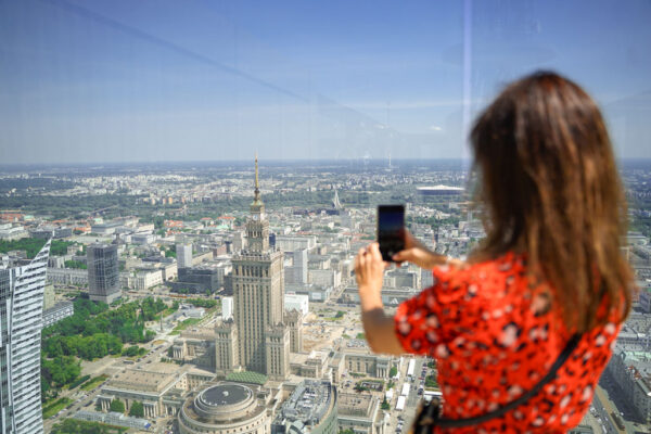 Panorama miasta z tarasu widokowego na budynku Varso, kobieta w czerwonej sukience robi zdjęcie smartfonem.
