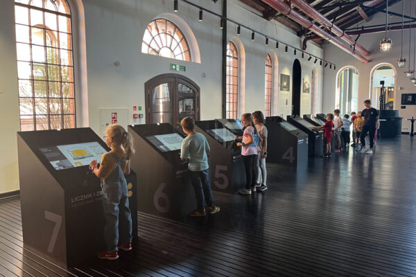 Sala ekspozycyjna Muzeum Gazowni Warszawskiej, ekrany multimedialne, przy których stoją dzieci.