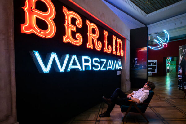Muzeum Neonów, mężczyzna siedzący na fotelu ogląda kolorowe neony zawieszone na ścianach.