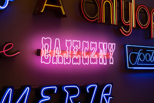 Muzeum Neonów, na ścianach wiszą kolorowe neony. Widoczny napis - Bajeczny oraz Społem