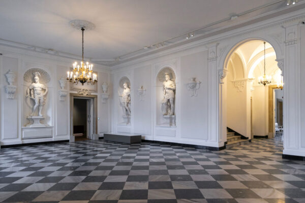 Wnętrza Pałacu Rzeczypospolitej, białe ściany zdobione sztukateriami, w nawach rzeźby wojowników.