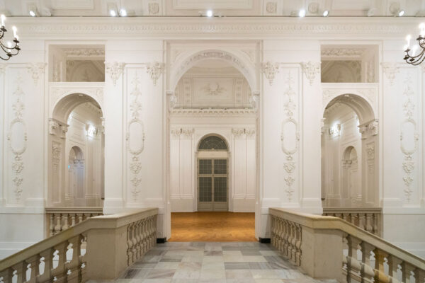 Wnętrza Pałacu Rzeczypospolitej, białe ściany zdobione sztukateriami, po bokach kamienne balustrady schodów.