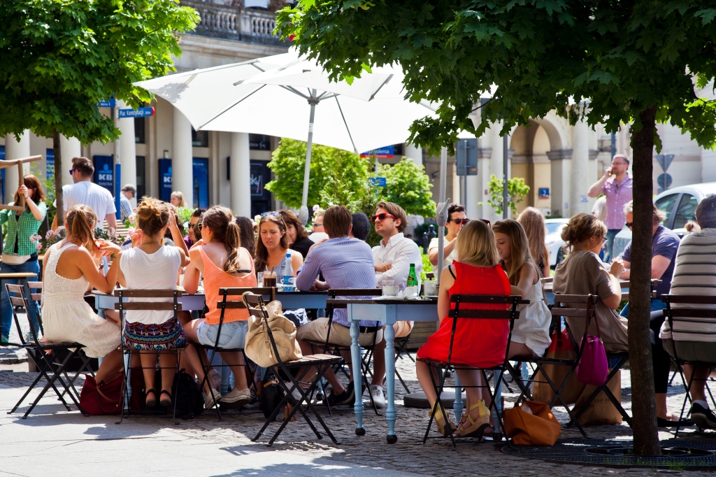 Ogródek restauracyjny na Placu Zbawiciela, ludzie siedzą przy stolikach, słoneczny dzień, lato.